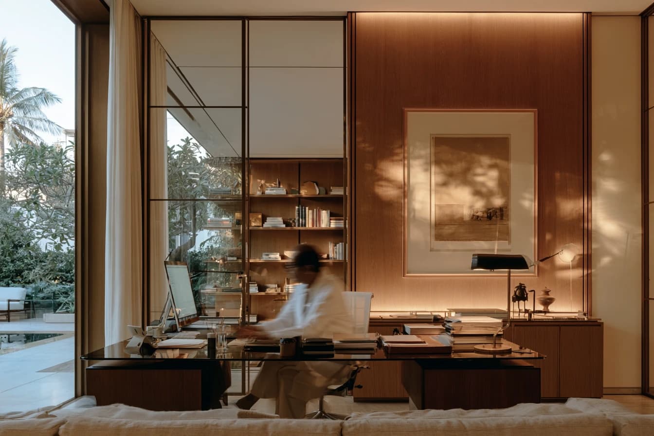 A physician at a desk reading, a garden beyond the glass