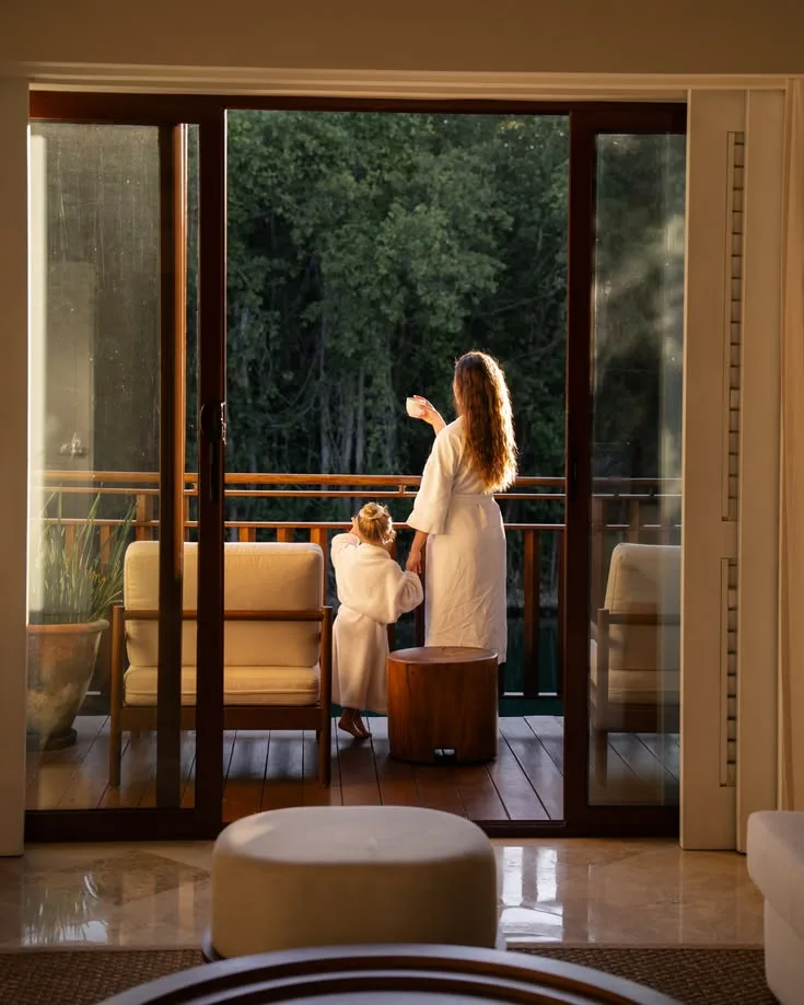 A mother and child on a balcony in the morning, trees beyond
