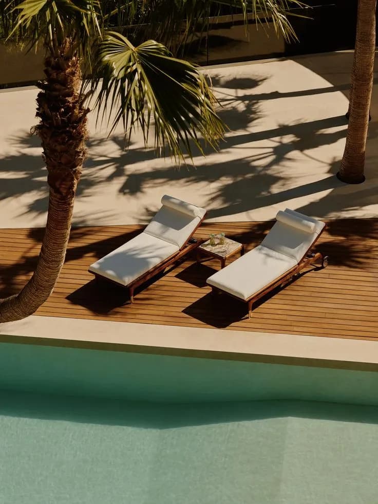 Two loungers on a deck beside a pool, in the shade of palms