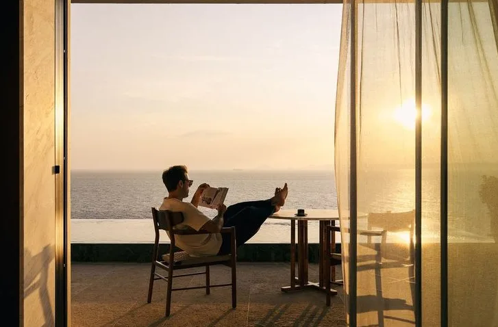 A man reading on a terrace at sunset, the sea beyond