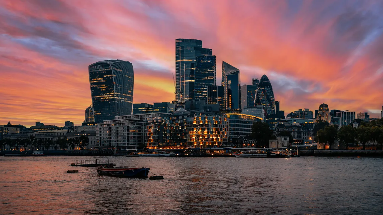 The towers of the City of London under a streaked pink sunset, seen across the Thames