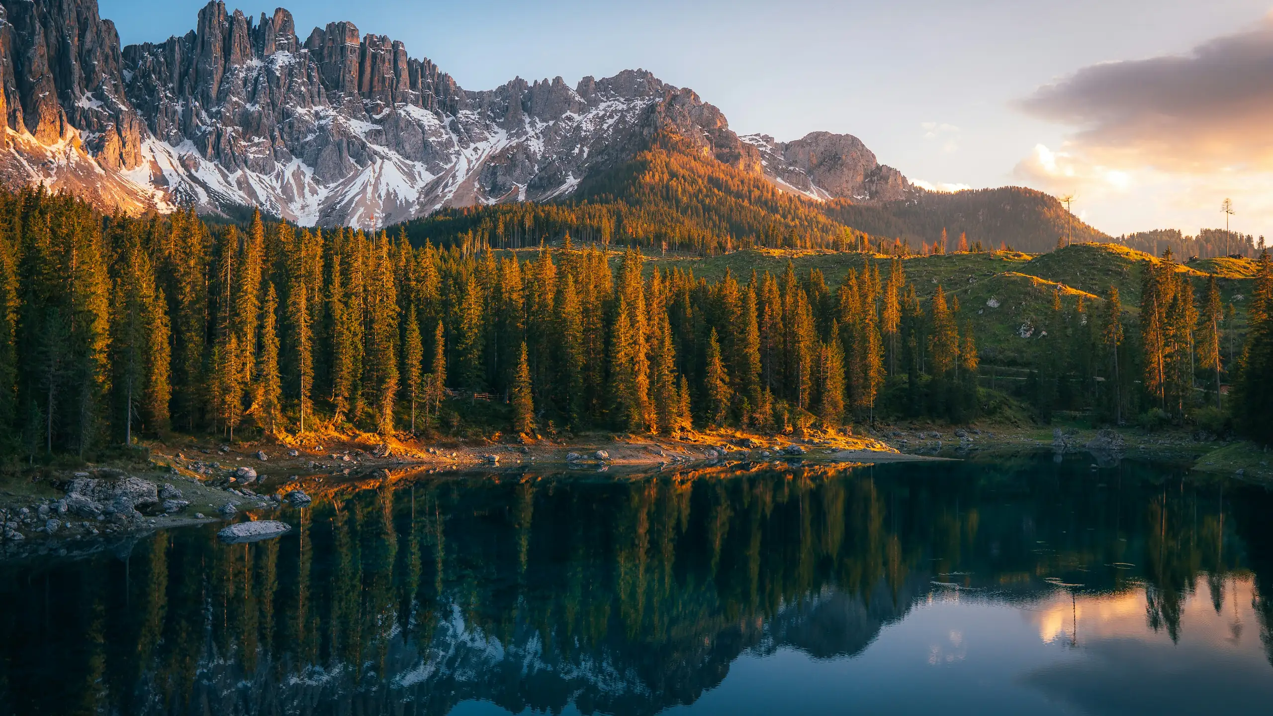 Pine forest and jagged Dolomite peaks reflected in a clear lake at sunset