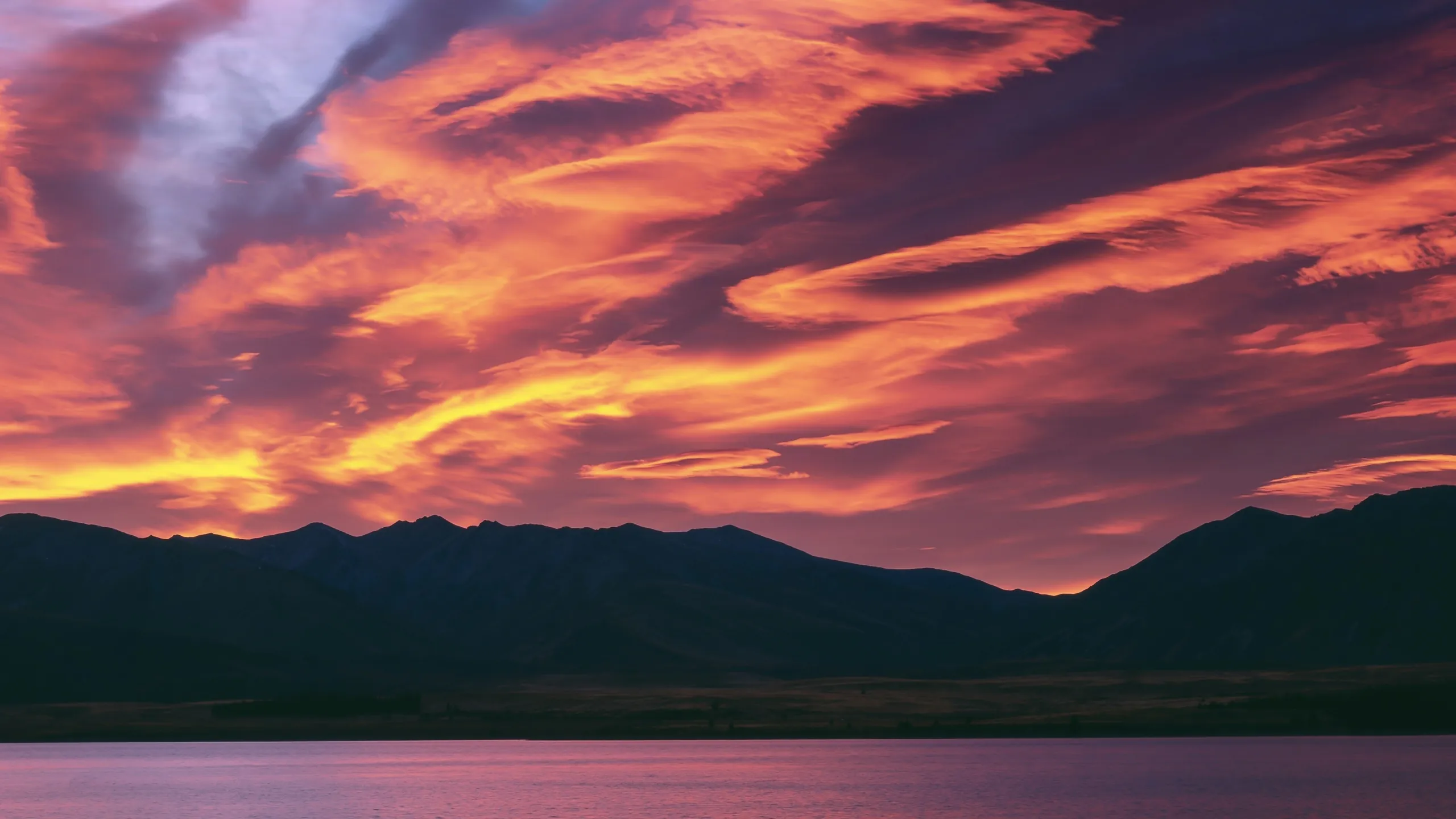 A sky of red and orange cloud at dawn over a dark mountain lake