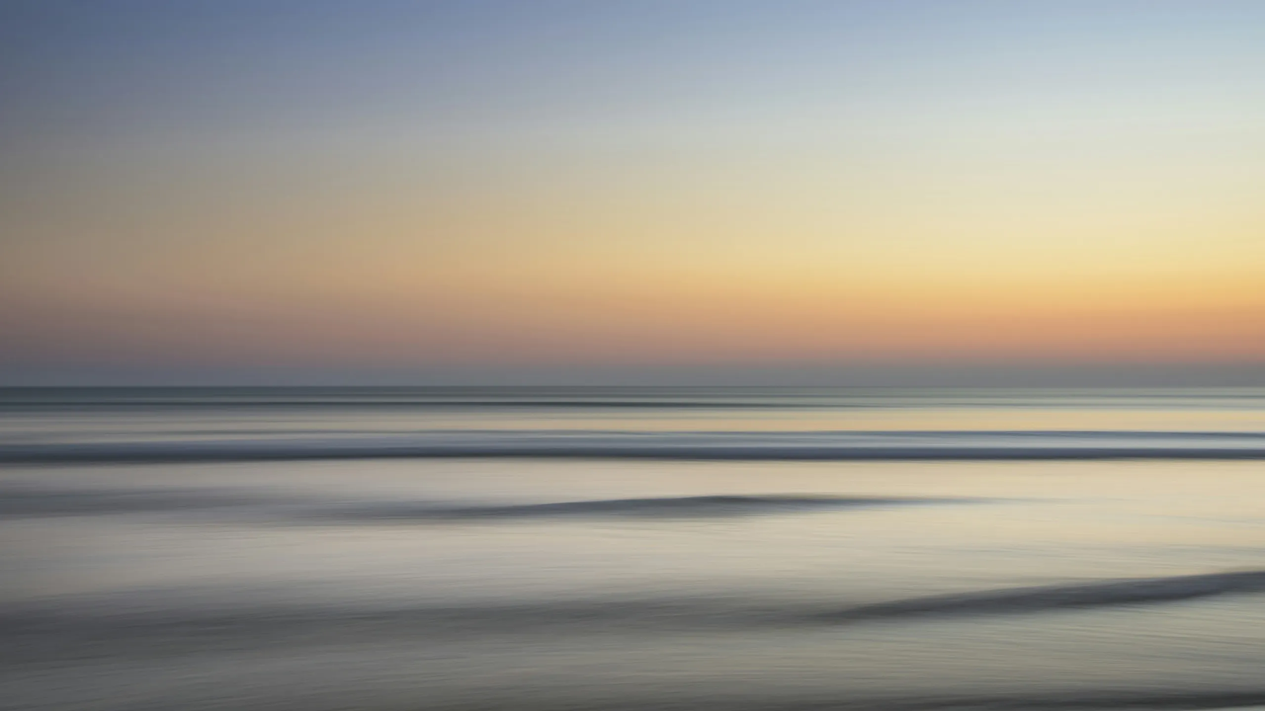 A calm sea under bands of gold and grey cloud, smoothed by a long exposure