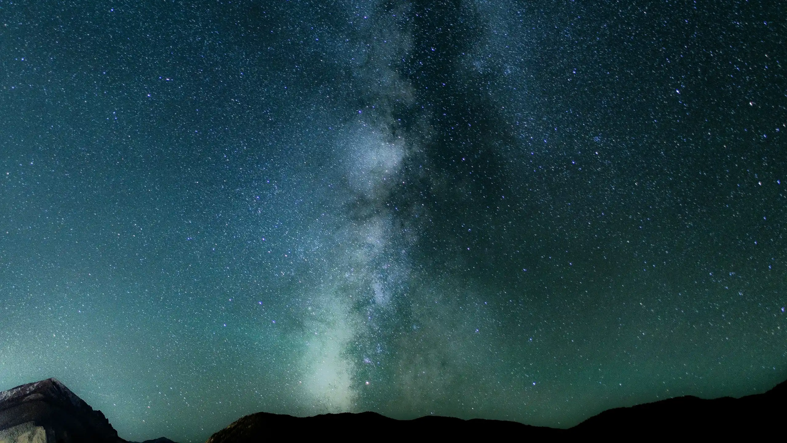 The Milky Way rising in a green and blue night sky above dark hills