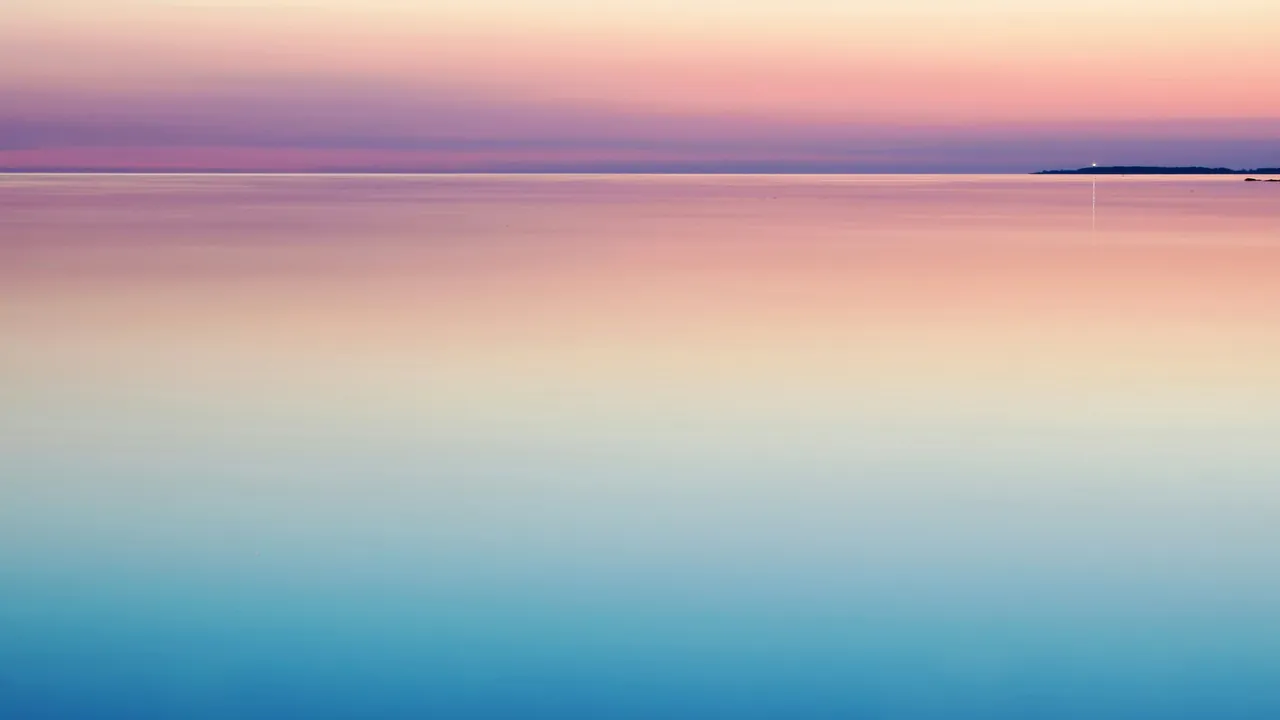 A flat calm sea fading from blue to a pink horizon