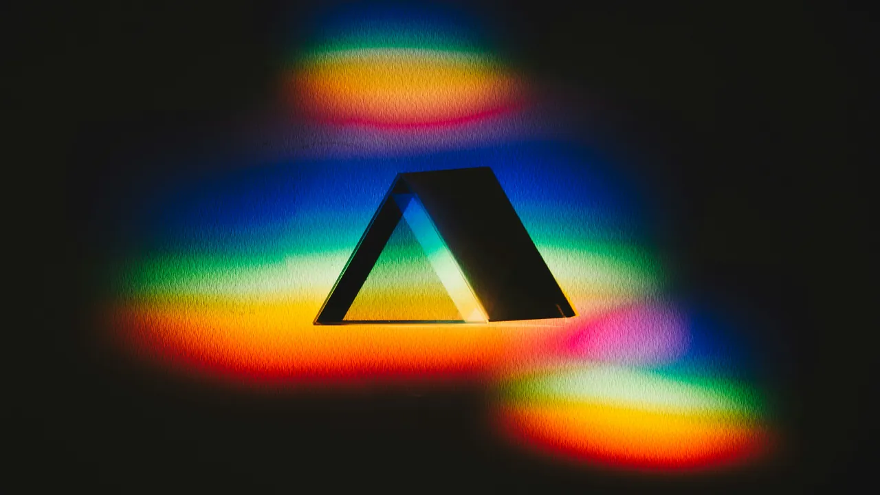 A glass prism on black, casting rings of rainbow light