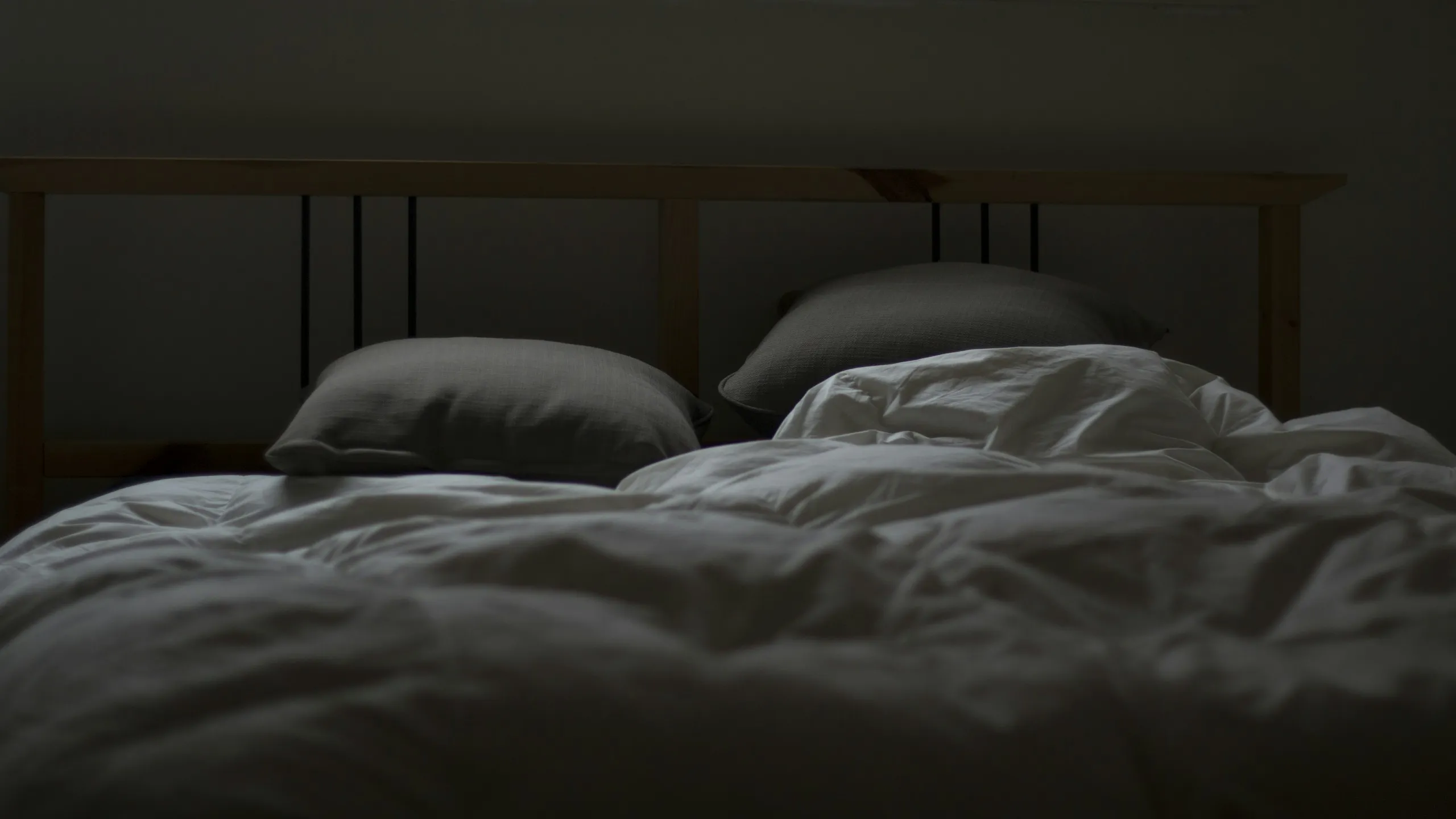 An empty bed with rumpled grey linen in a dim, quiet bedroom