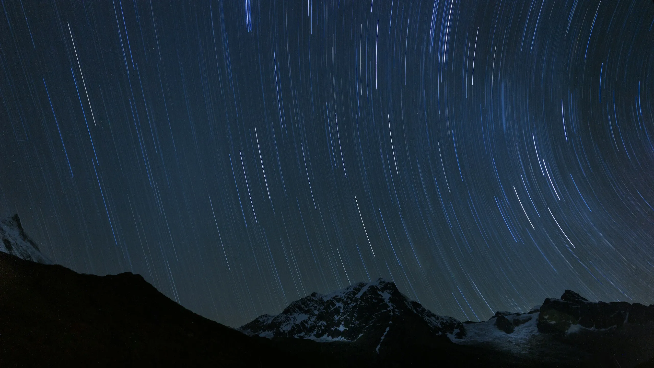 Star trails curving across the night sky above snow-capped mountains