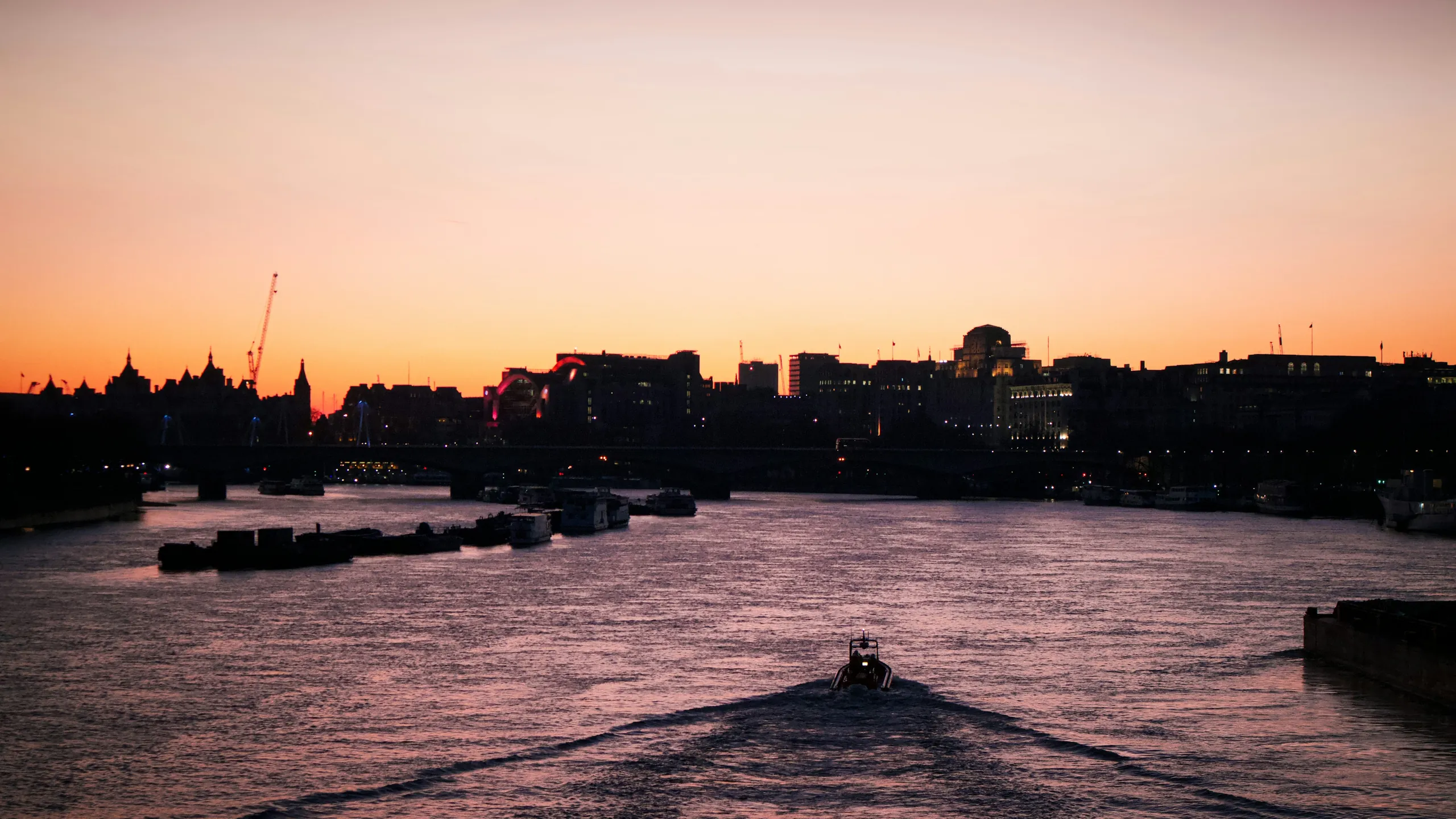 A small boat on the Thames at dusk, the skyline in silhouette against a pink sky