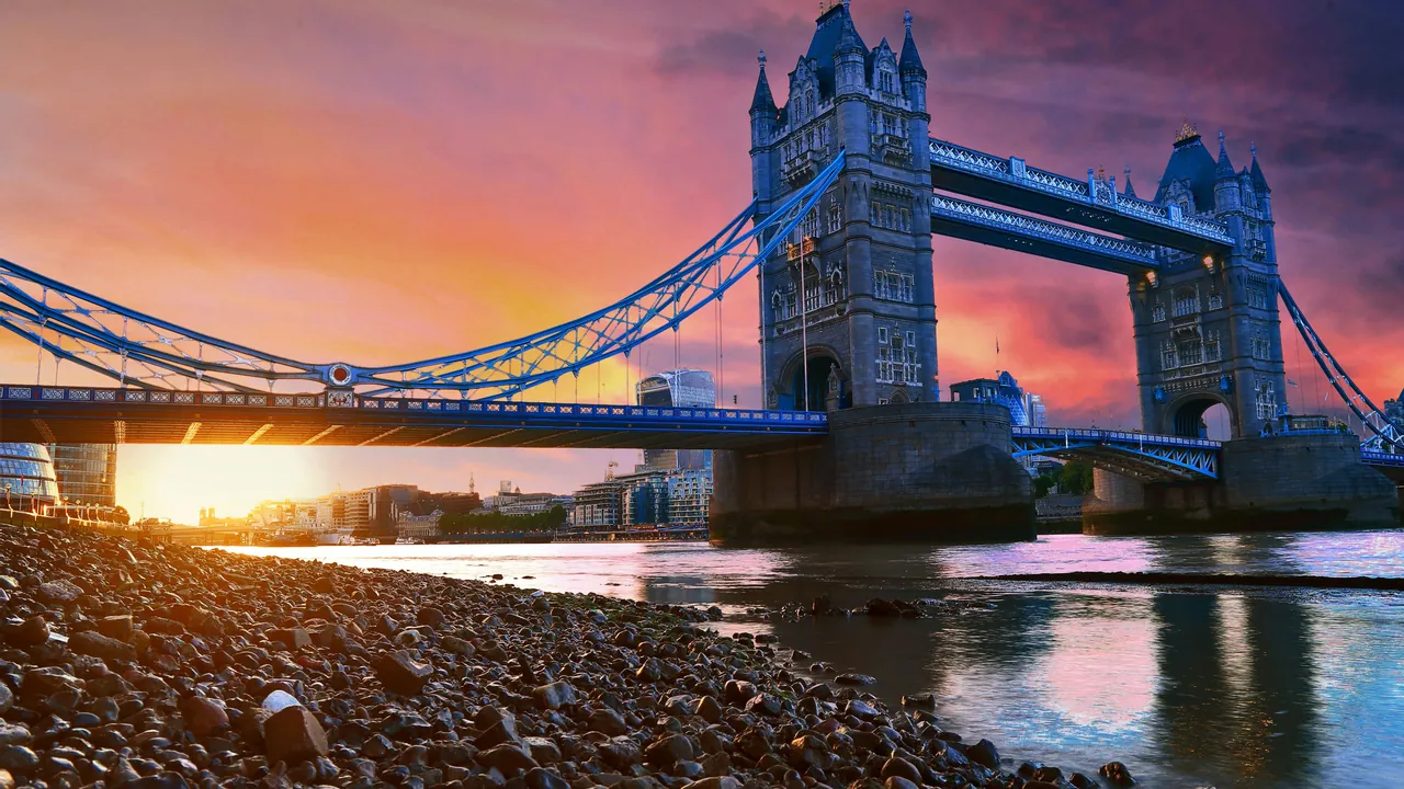 Tower Bridge at sunset from the pebble foreshore, the sky orange and violet
