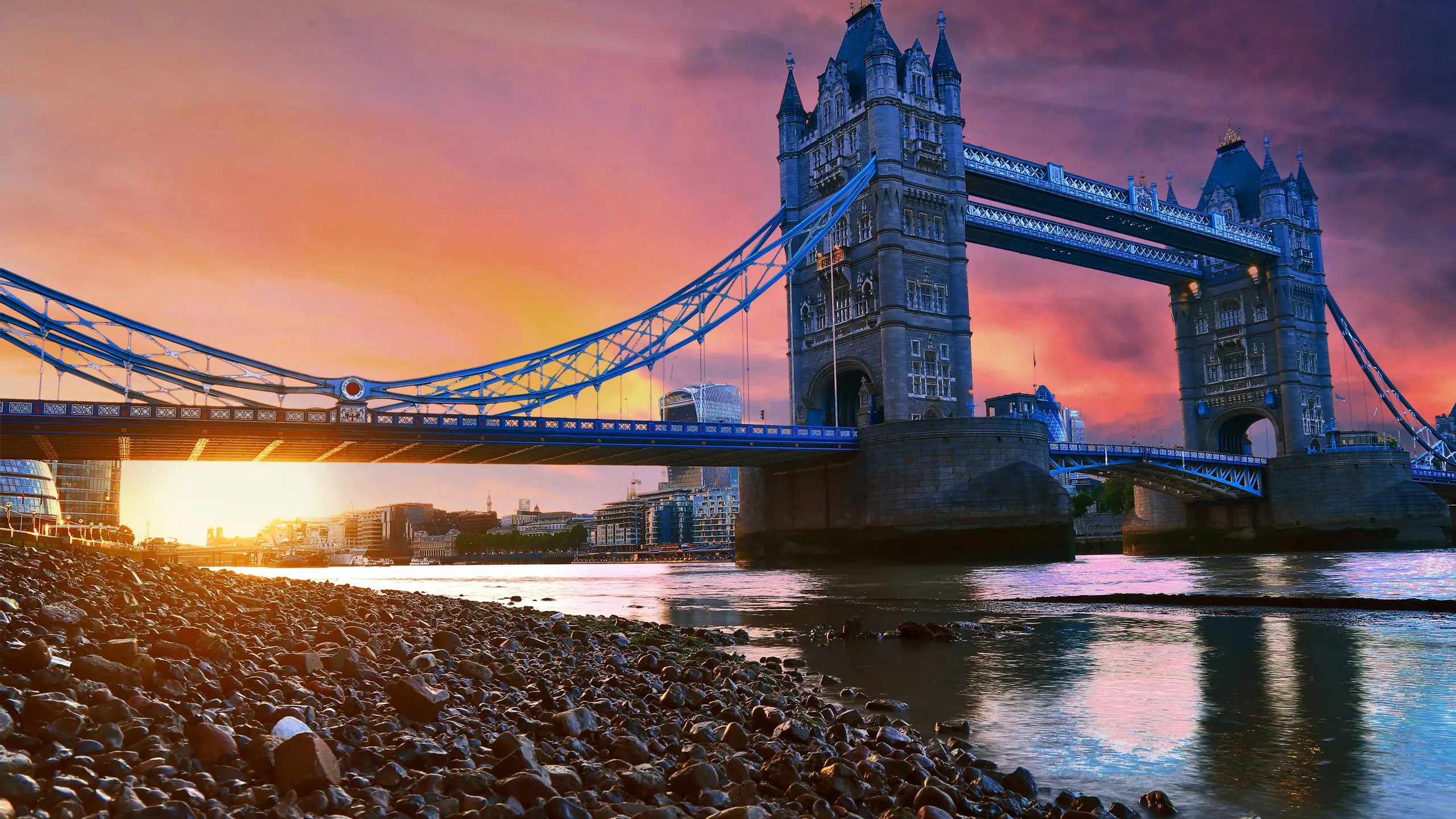 Tower Bridge at sunset from the pebble foreshore, the sky orange and violet