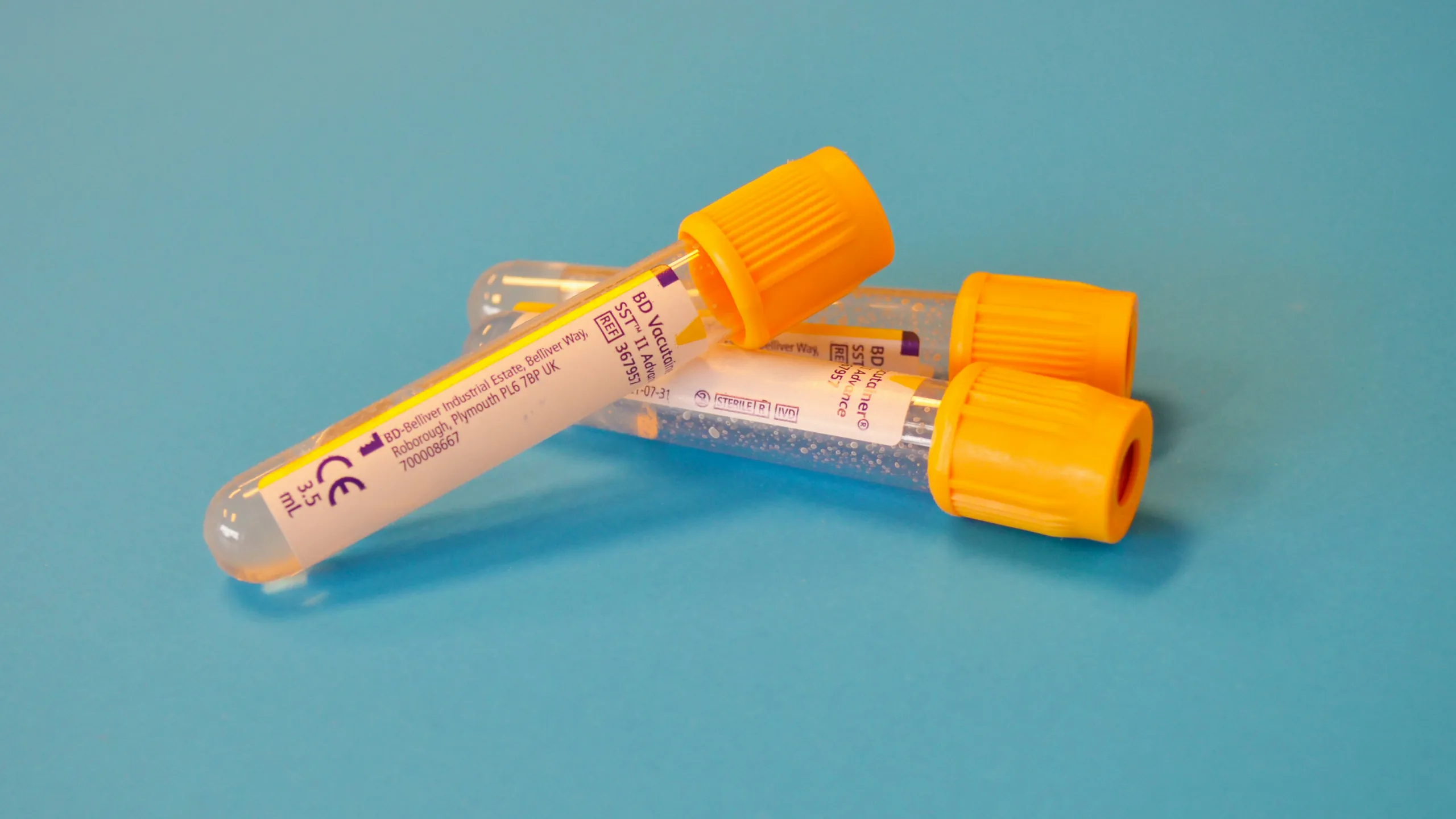 Two sample tubes with orange caps lying on a teal surface