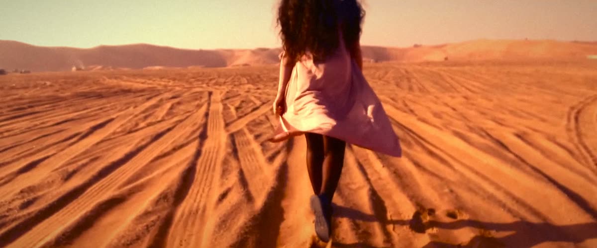 A woman in a pink dress running across red dunes