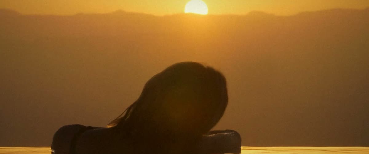 A woman resting at the edge of an infinity pool at sunset